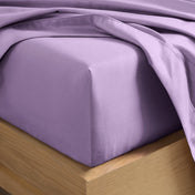 A close-up of a fitted sheet covering the corner of a bed frame, with matching top sheet draped over it.