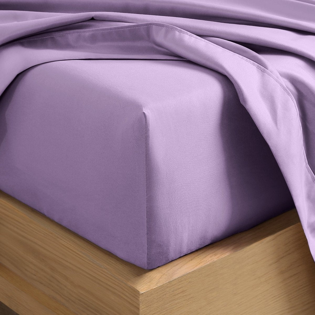 A close-up of a fitted sheet covering the corner of a bed frame, with matching top sheet draped over it.
