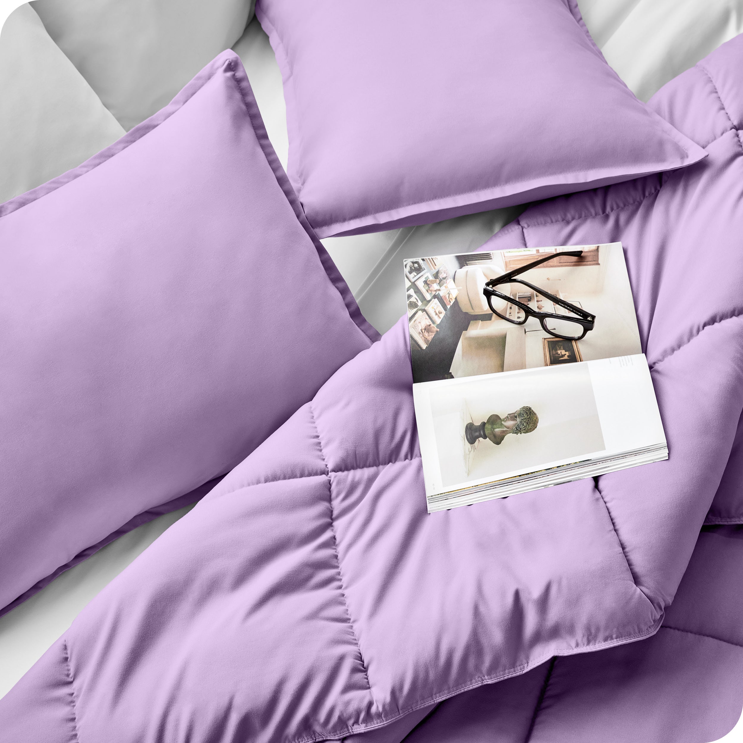 Close up of a comforter set on a bed. There are glasses and a magazine on top of the comforter.