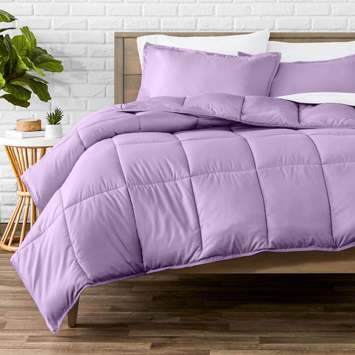 Comforter set on a bed with a white brick wall and plant in the background
