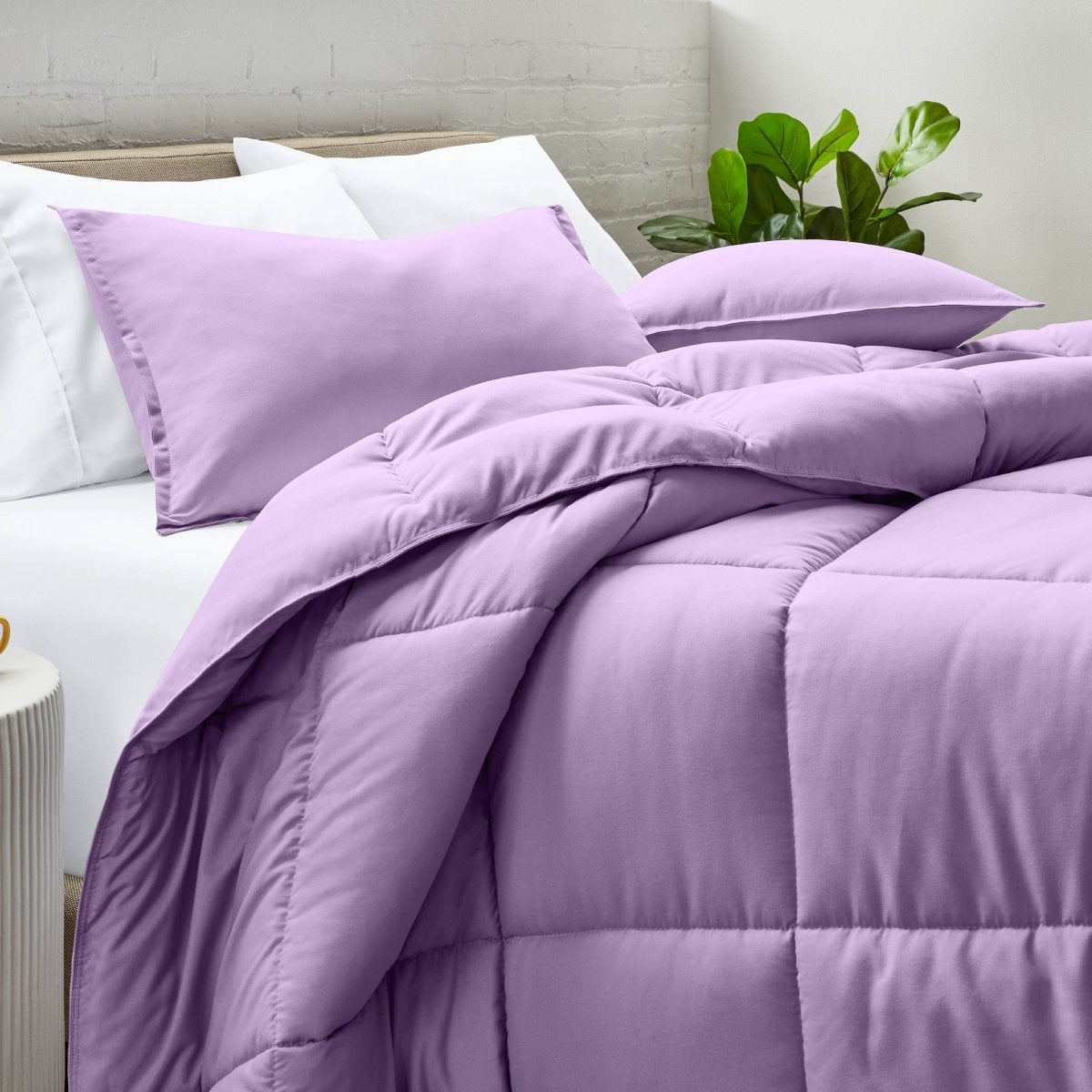 Comforter and pillow shams on a bed with a white brick wall and plant in the background