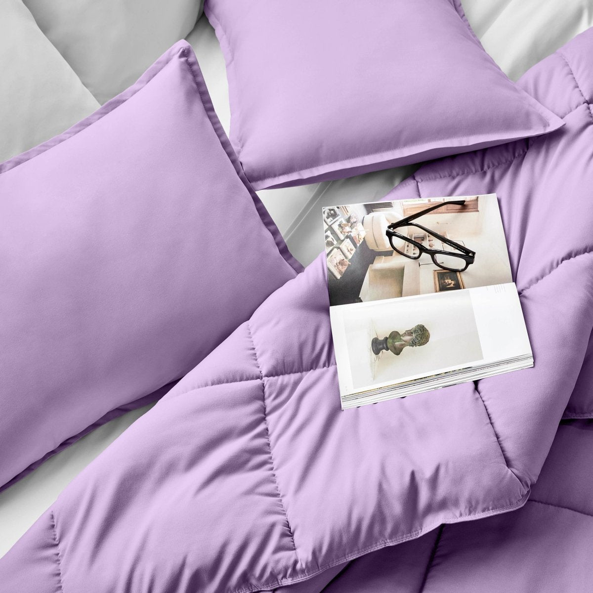 Comforter and pillows on a bed with a magazine and glasses.