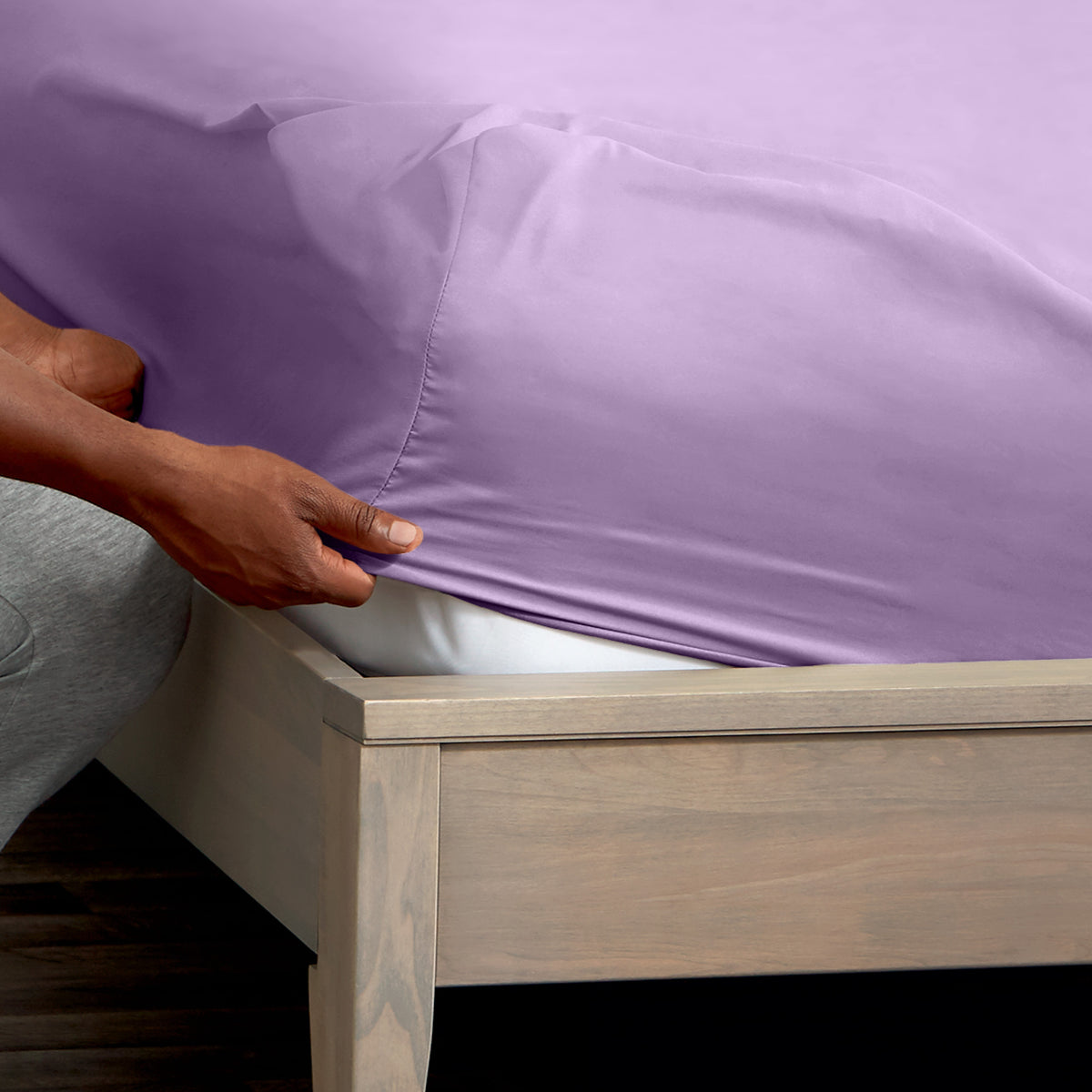 A man is putting a fitted sheet on a bed
