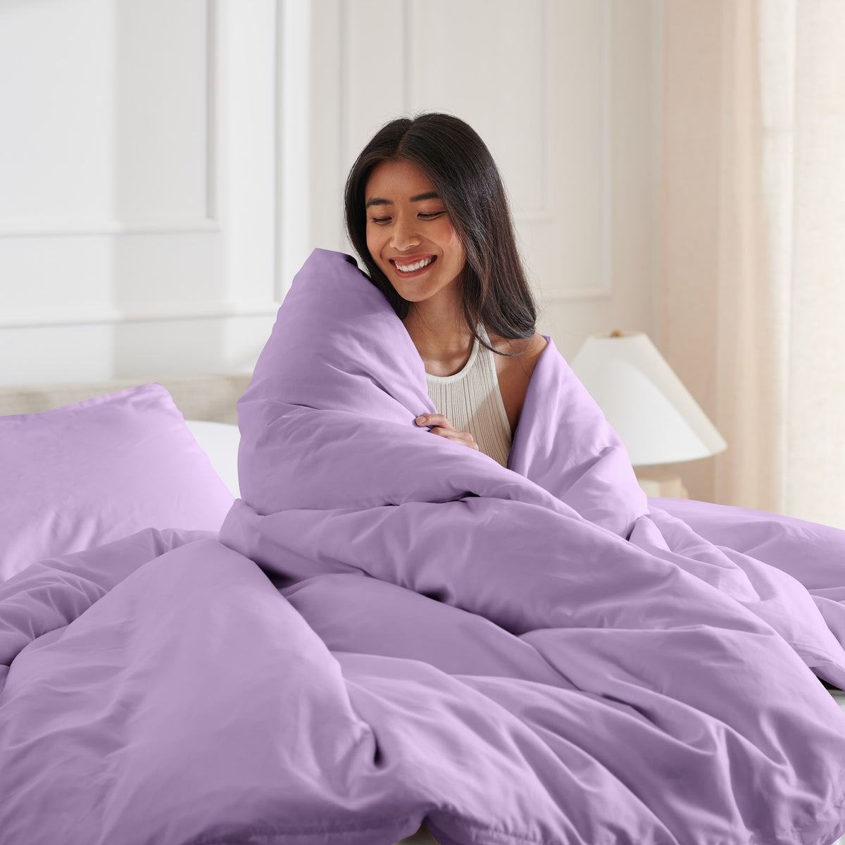 Woman smiling under duvet cover set in a bedroom setting