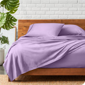 A wooden bed frame with a microfiber sheet set on the mattress.