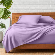 A wooden bed frame with a microfiber sheet set on the mattress.