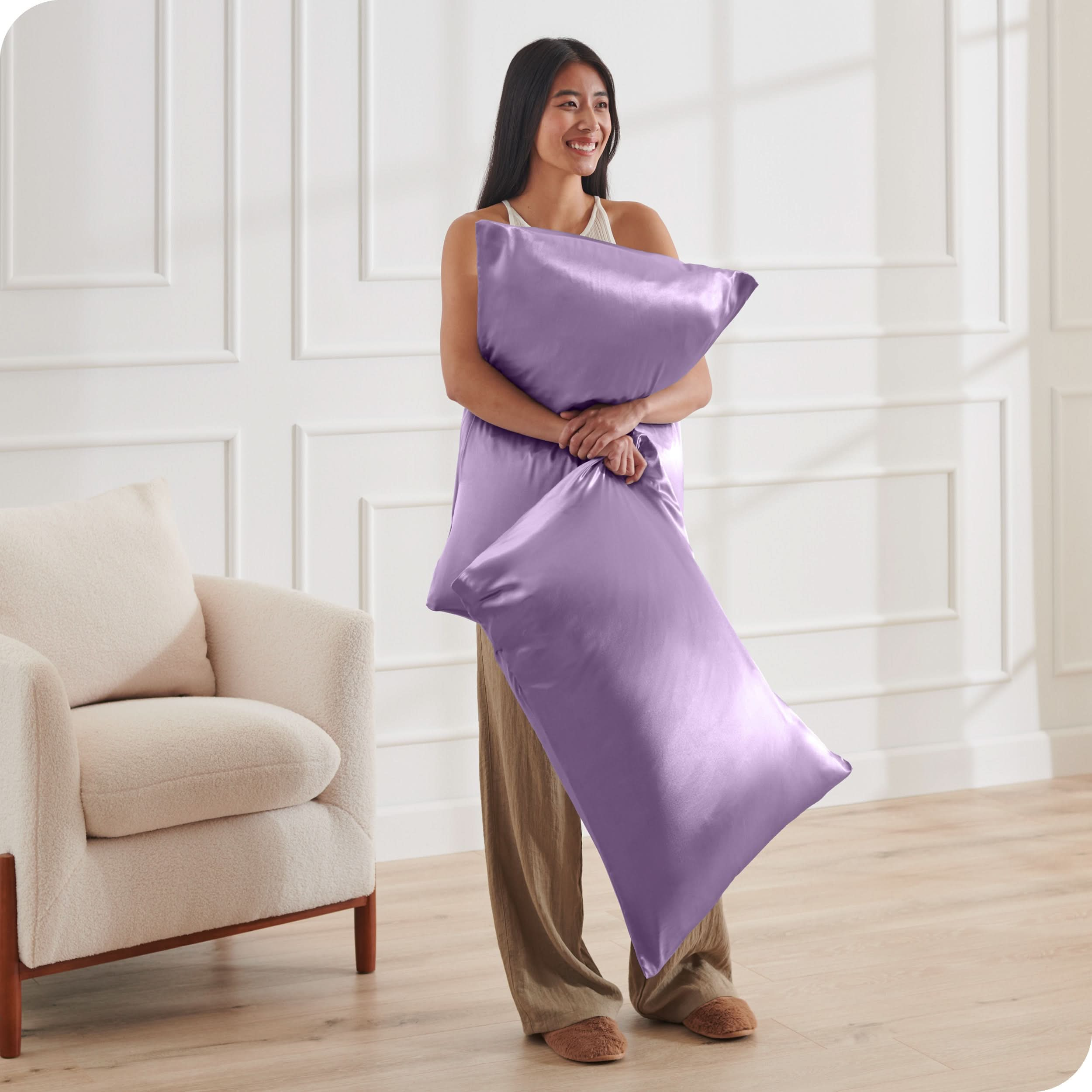 A woman has 2 pillows in her hands and they have satin pillowcases on them