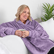 A woman sitting on a couch holding a mug wearing a sherpa blanket.