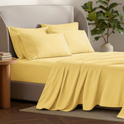 Bed sheets and pillows on a bed with a plant and side table in the background.