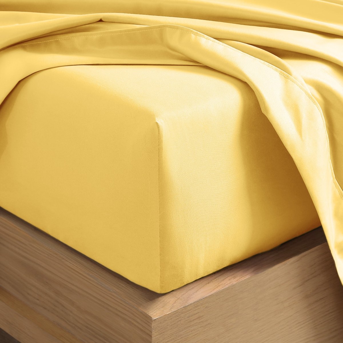 A close-up of a fitted sheet covering the corner of a bed frame, with matching top sheet draped over it.