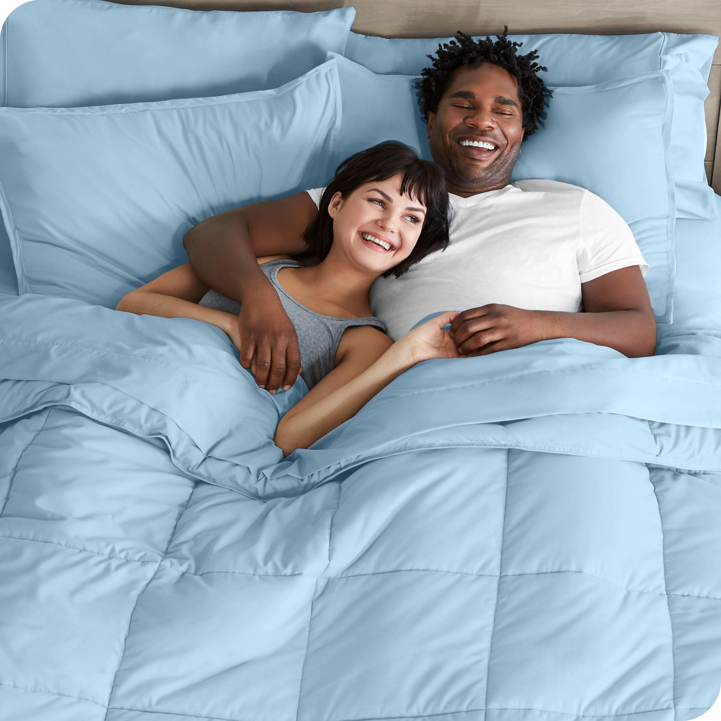 A couple is lying in bed with a comforter and sheets over them