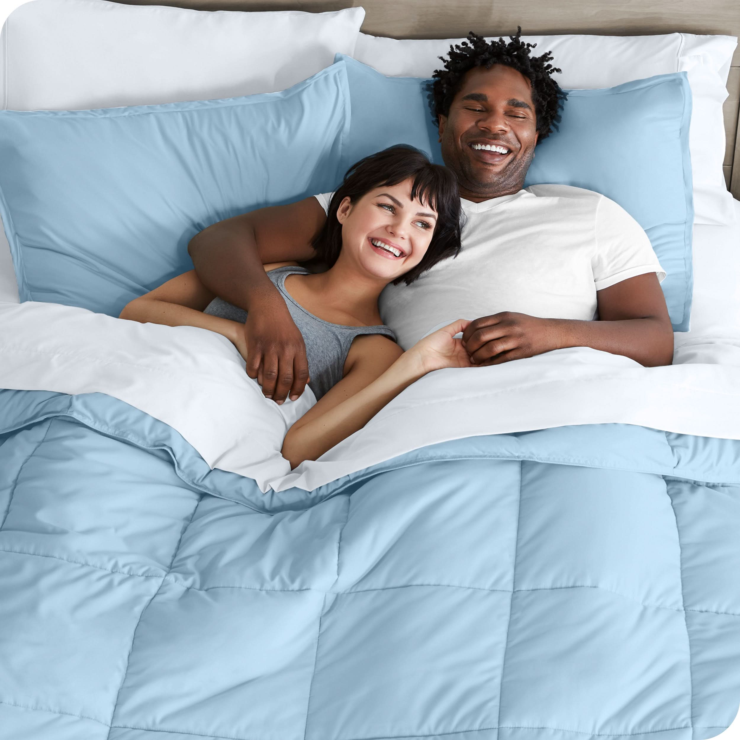 A couple is lying in bed with a comforter and sheets over them