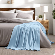 A cotton waffle blanket is on the corner of a bed. It is hanging down the side and end of the bed.