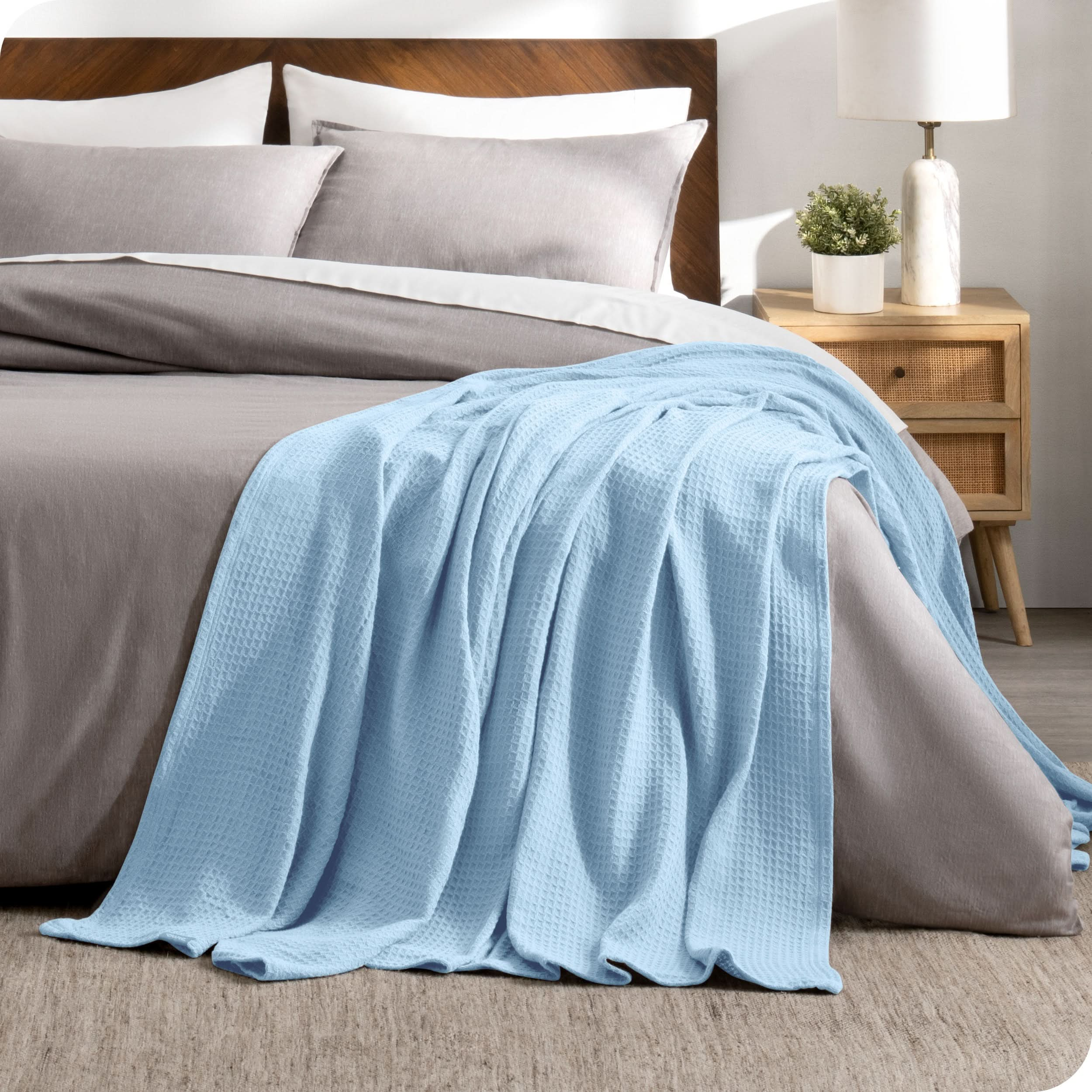 A cotton waffle blanket is on the corner of a bed. It is hanging down the side and end of the bed.