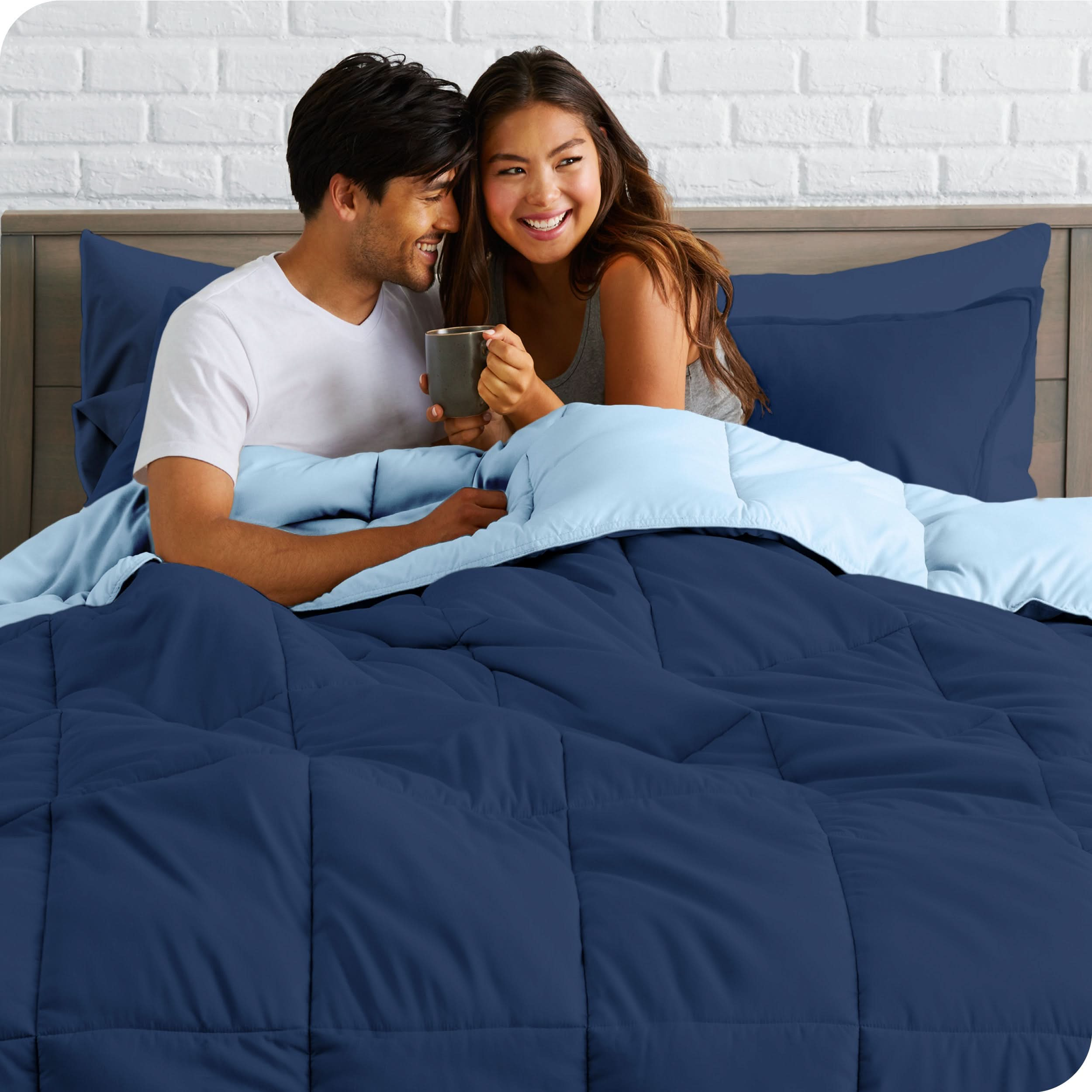 A couple sitting in a bed made with a reversible comforter and sheet set