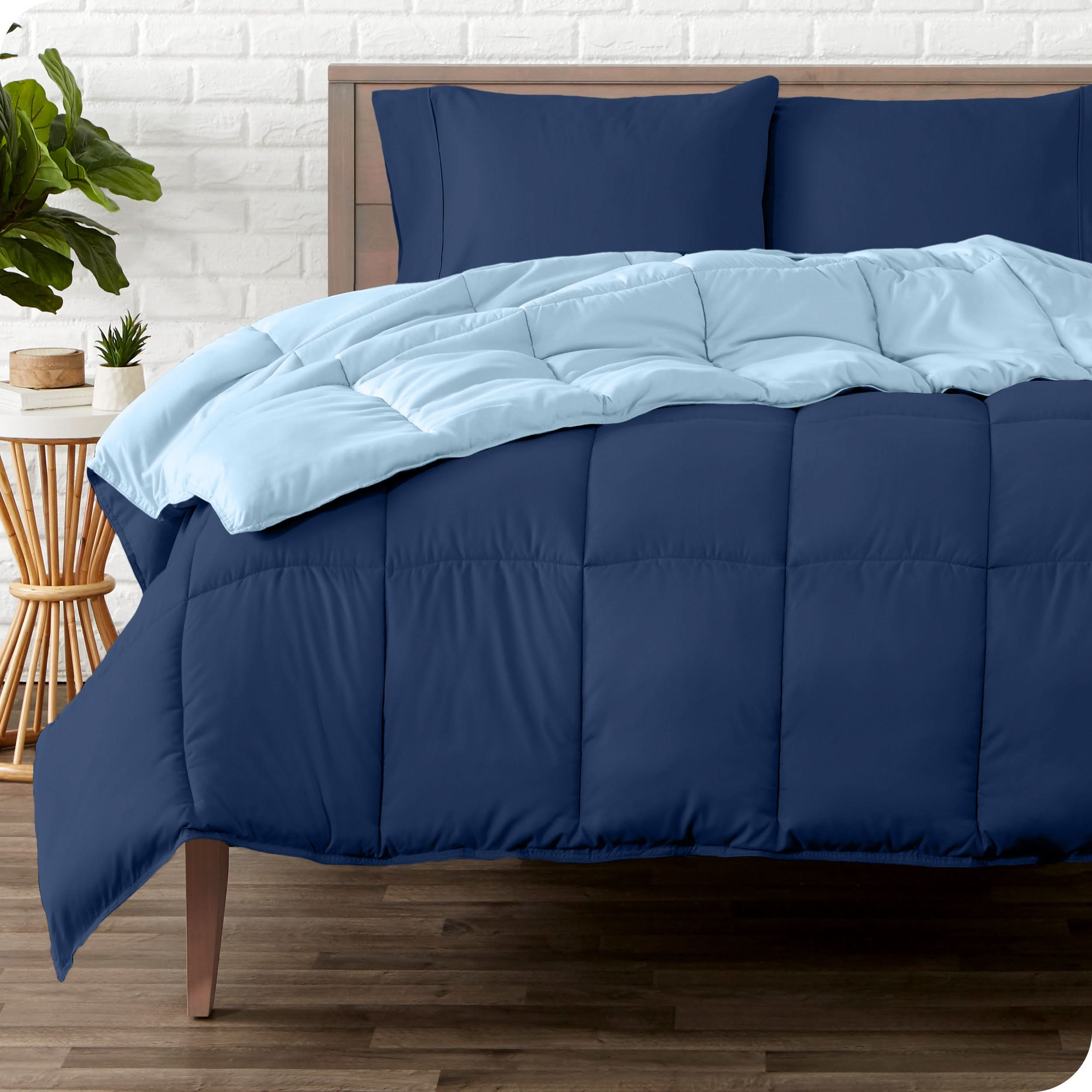 A wooden bed frame with a reversible comforter and sheet set on the mattress