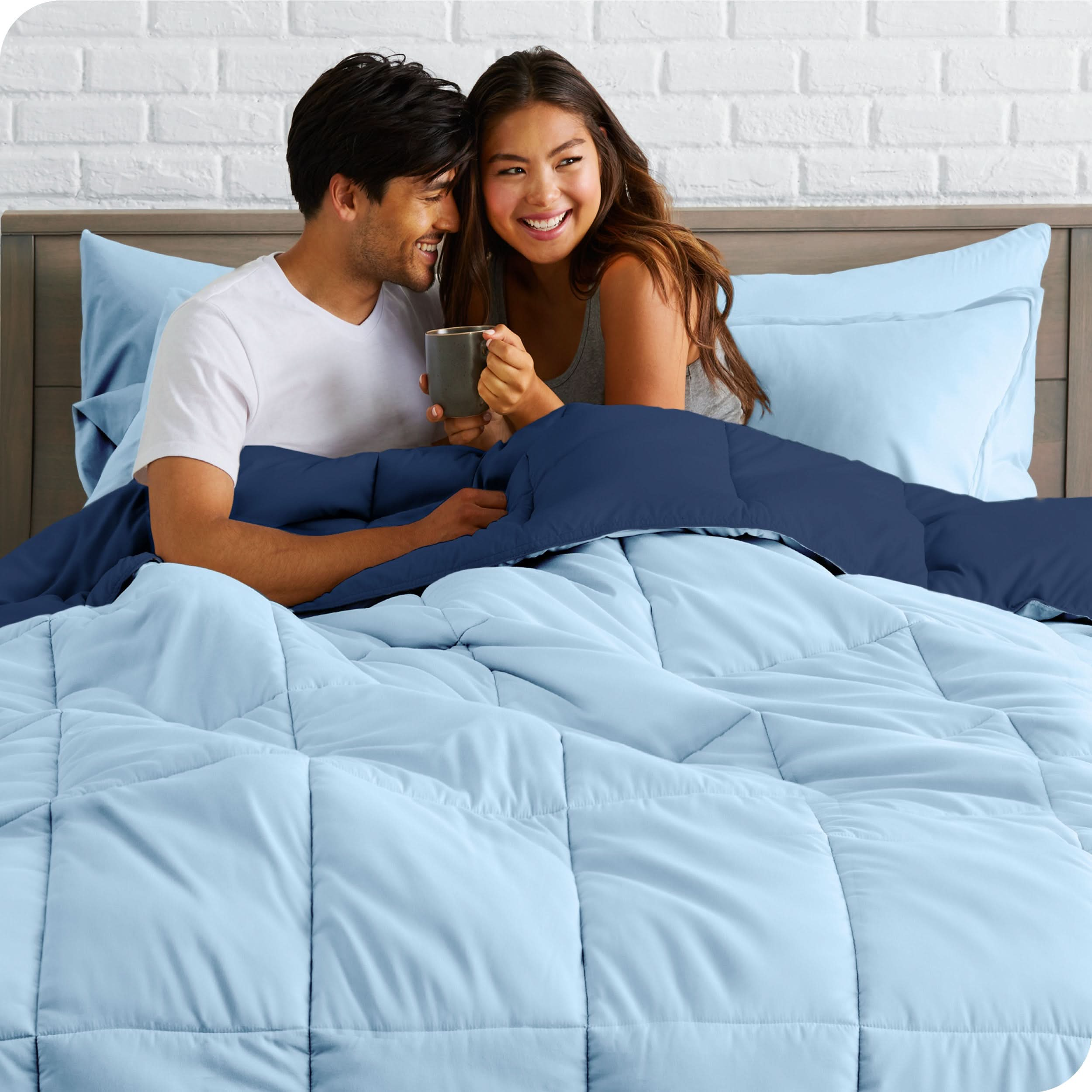 A couple sitting in a bed made with a reversible comforter and sheet set