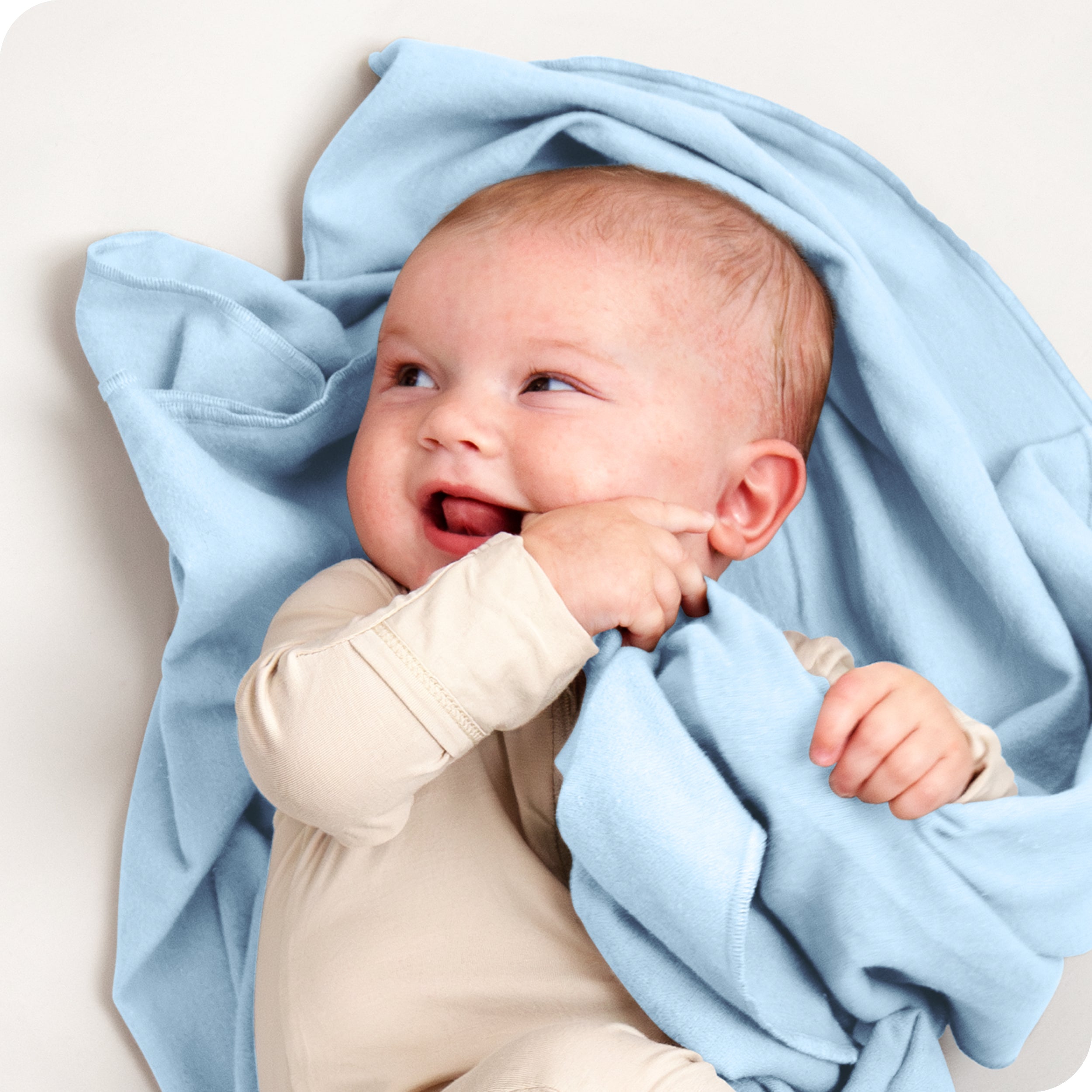 A baby lying on a receiving blanket. She has her thumb in her mouth.