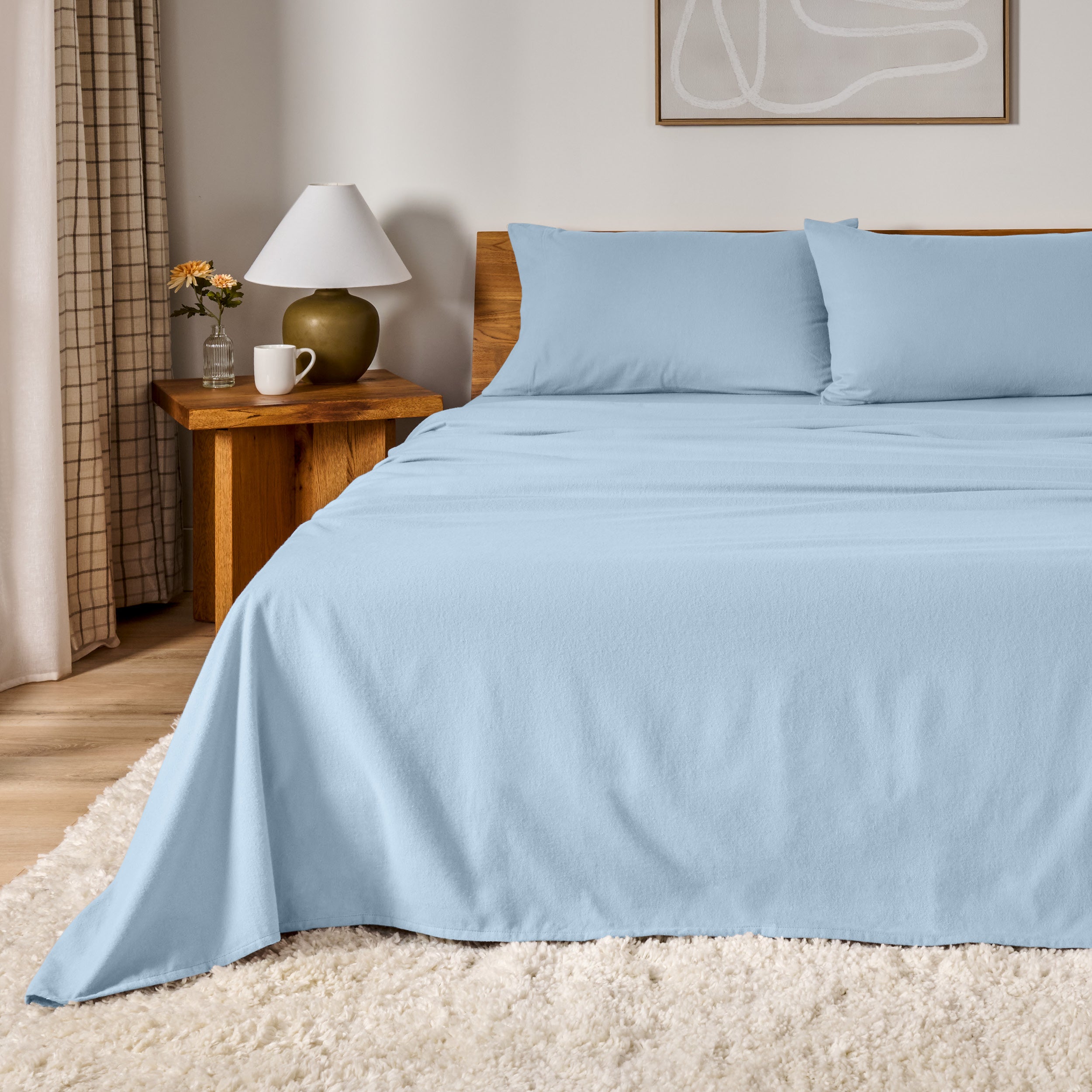 A bed dressed in flannel sheet set in a bedroom with a wooden headboard, bedside table and lamp