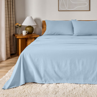 A bed dressed in flannel sheet set in a bedroom with a wooden headboard, bedside table and lamp