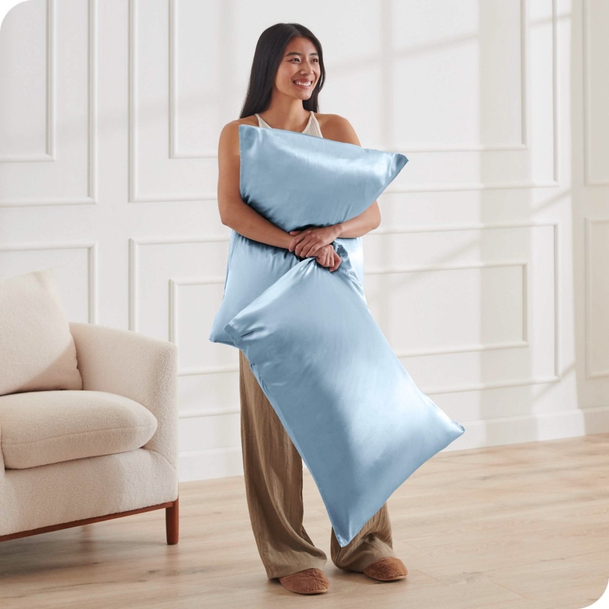 A woman standing while holding pillows with silk pillowcases on them