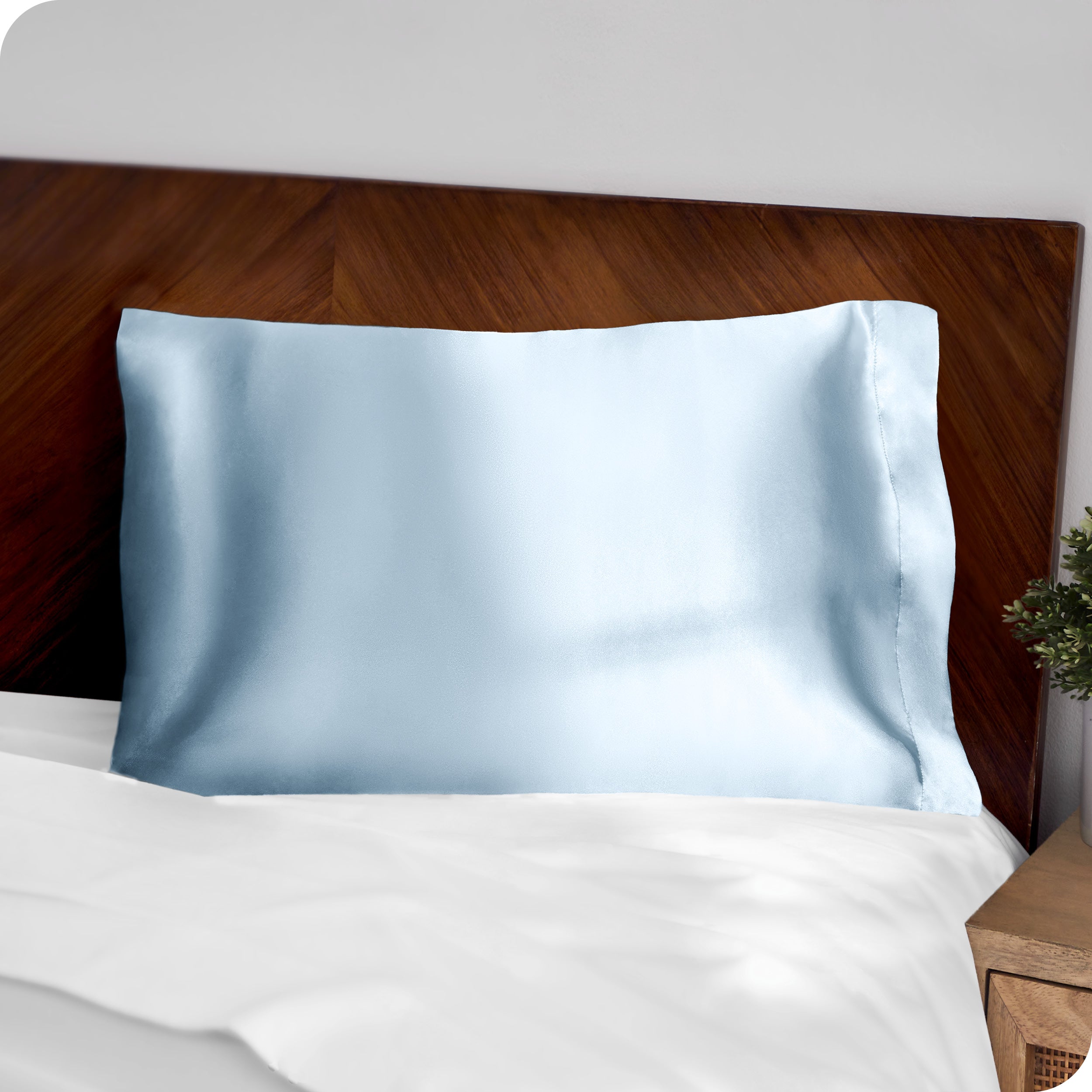 A blue silk pillowcase on a pillow resting on a headboard