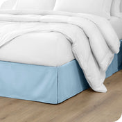 A modern bed with a microfiber bed skirt with pleats on the corners and midway on each side.