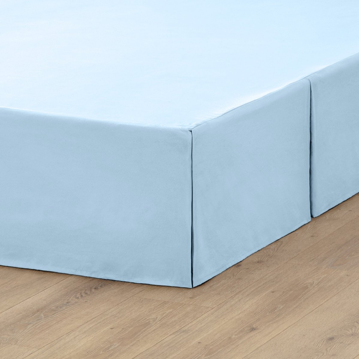 The corner of a box spring with a pleated bed skirt on it