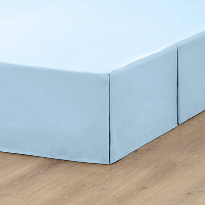 The corner of a box spring with a pleated bed skirt on it