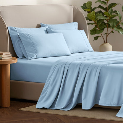 Bed sheets and pillows on a bed with a plant and side table in the background.