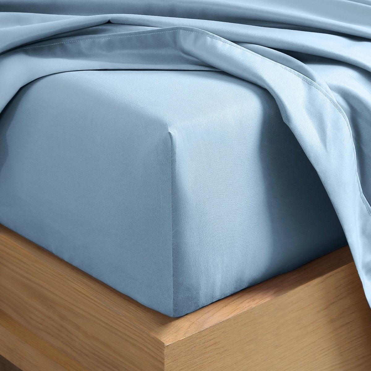 A close-up of a fitted sheet covering the corner of a bed frame, with matching top sheet draped over it.