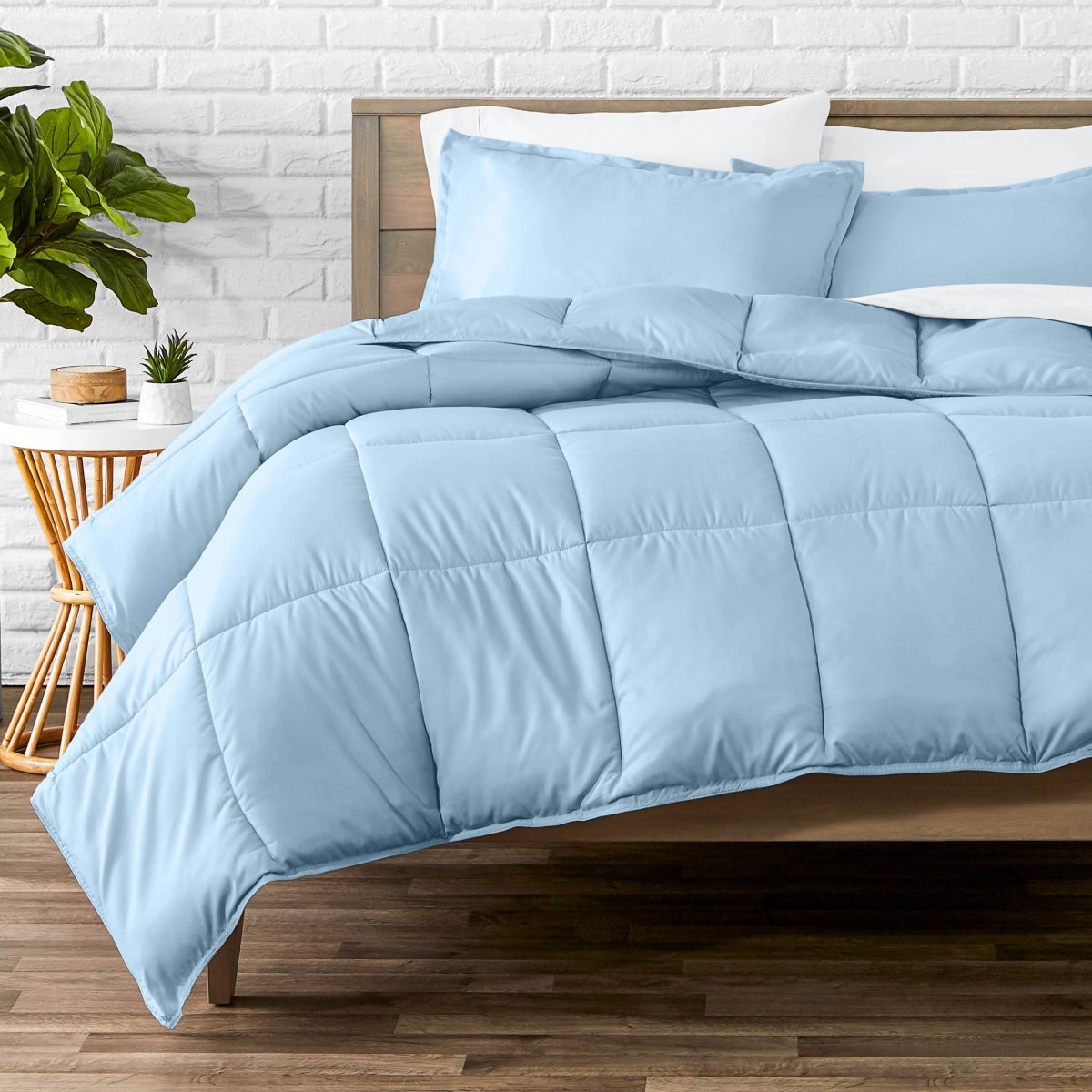 Comforter set on a bed with a white brick wall and plant in the background
