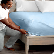 Man is kneeling while putting a fitted sheet on a mattress