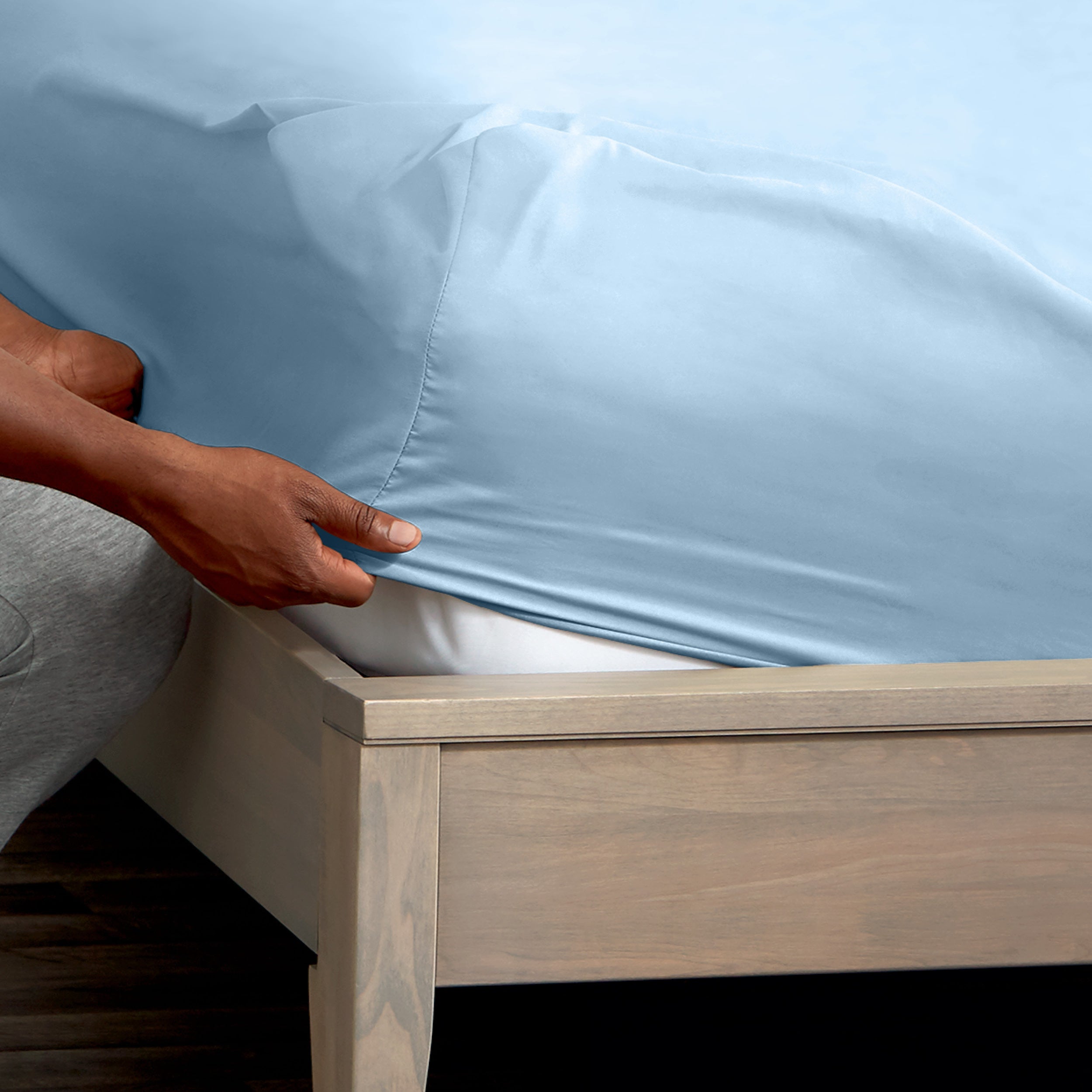 A man is putting a fitted sheet on a bed