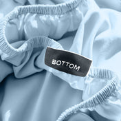 A close-up of a fitted sheet with a label printed with the word 'BOTTOM' in white.