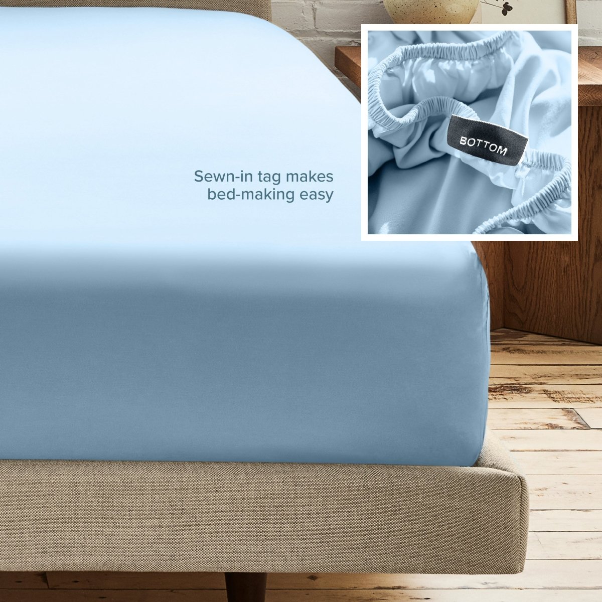 A fitted bed sheet on a bed frame with a small inset close-up of the elastic and a sewn-in tag labeled BOTTOM. White text on the sheet reads, 'Sewn-in tag makes bed-making easy.