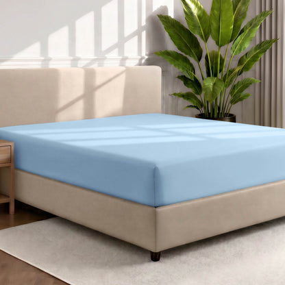 Bed with a fitted sheet in a room with a large plant and rug
