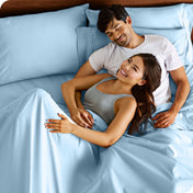 A couple is relaxing in bed with pillows behind them