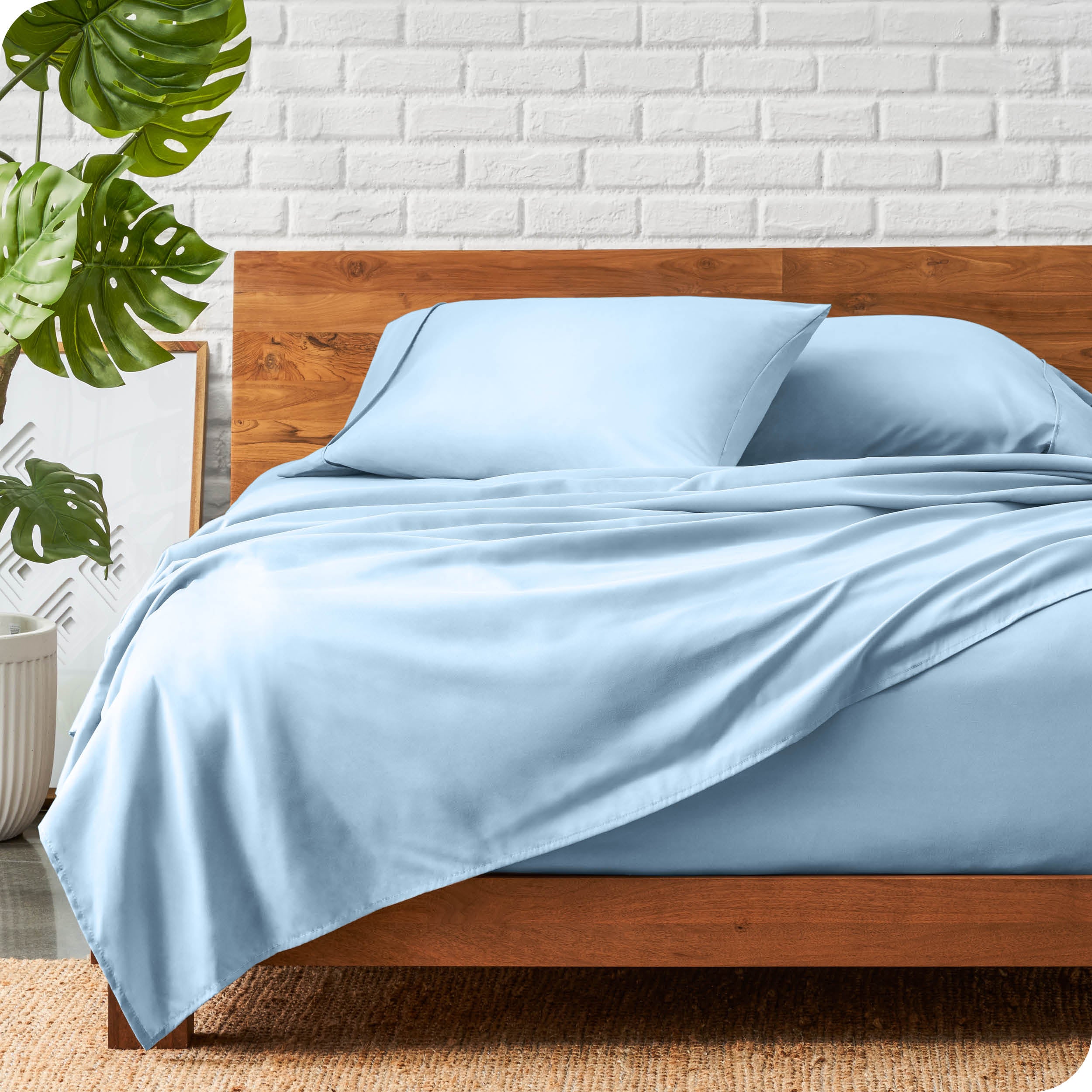 A wooden bed frame with a microfiber sheet set on the mattress.