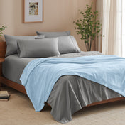 A bed made with grey sheets and a microplush blanket