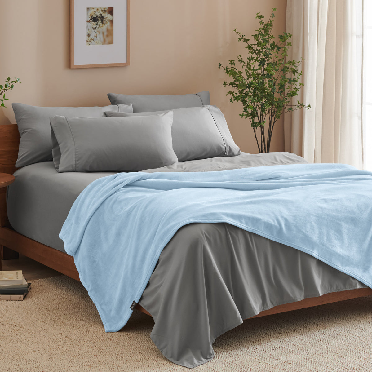 A bed made with grey sheets and a microplush blanket