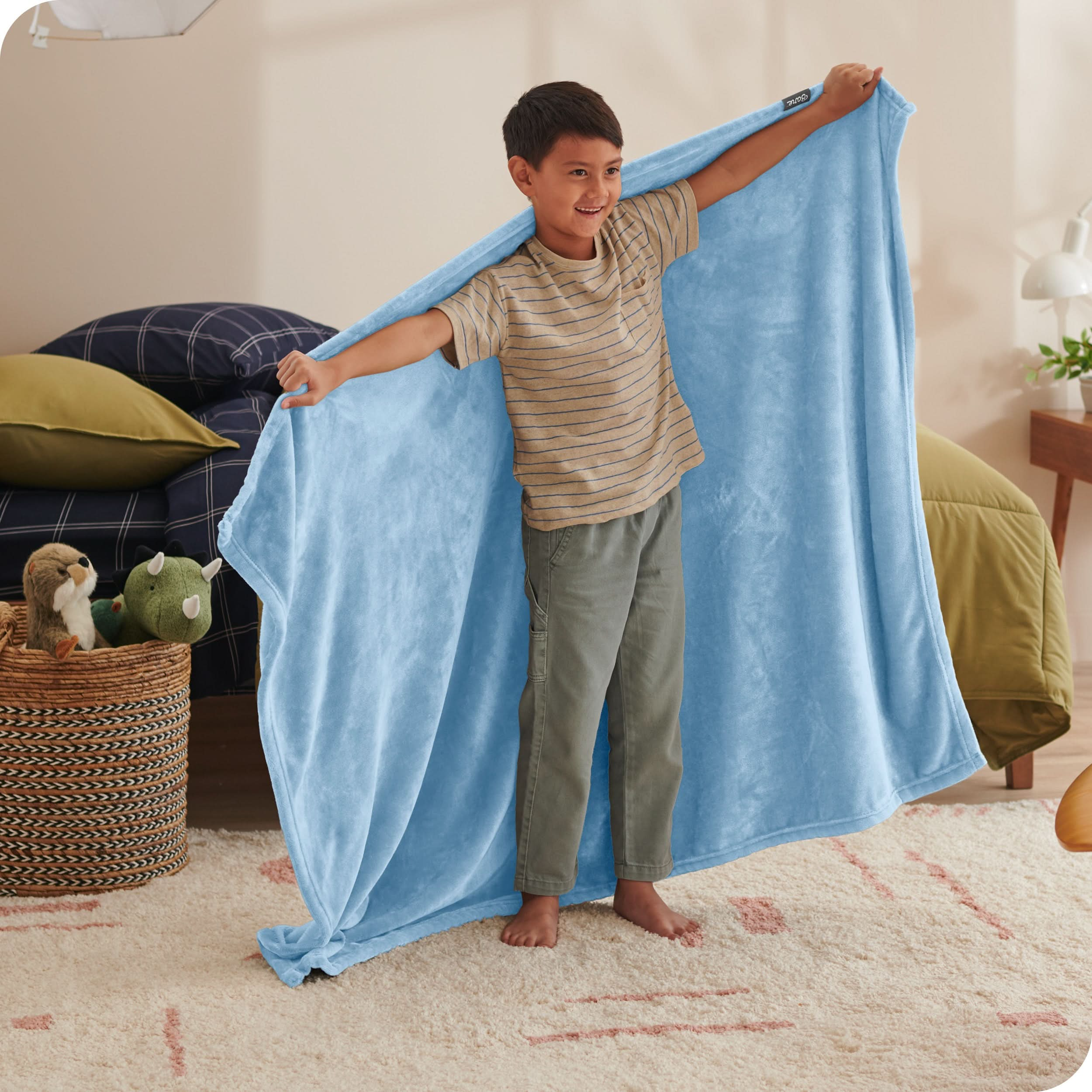 A child has his arms stretched out while holding a microplush blanket behind him