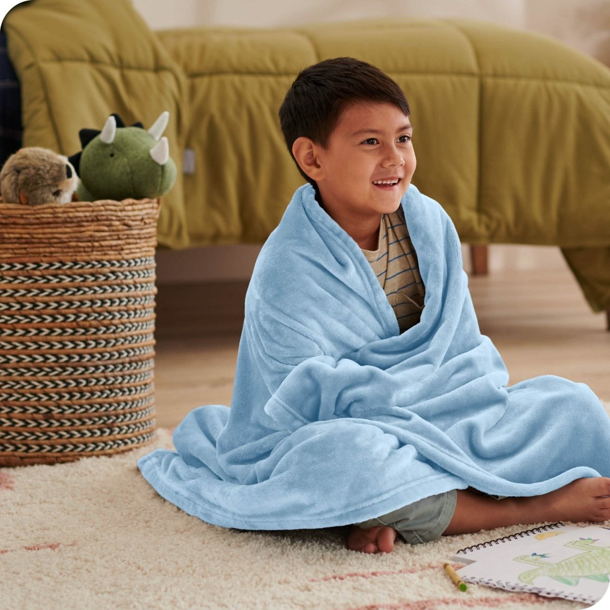 A boy is sitting on the floor of his bedroom with a microplush blanket wrapped around him