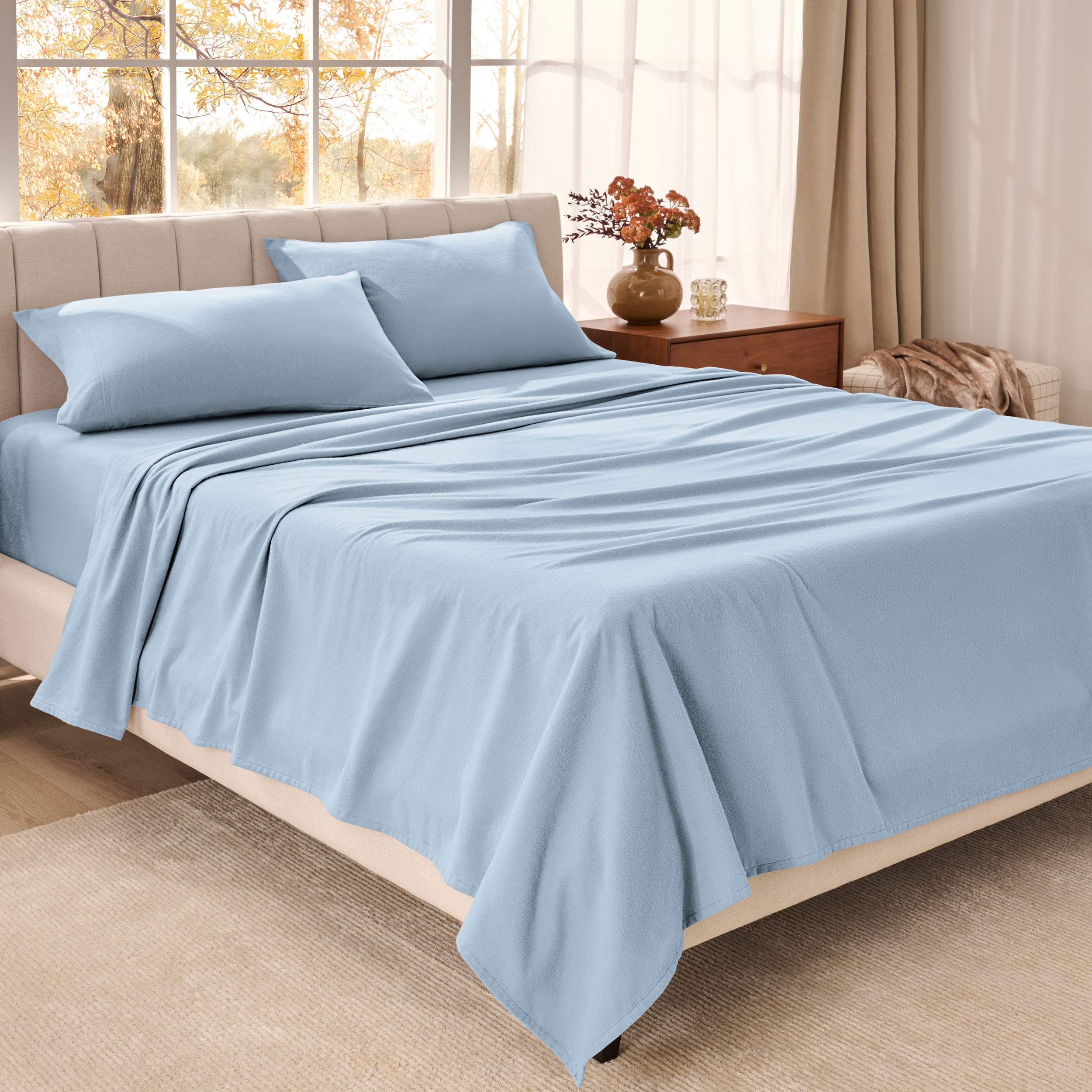 Bed sheets on a neatly made bed in a bright bedroom with large windows.
