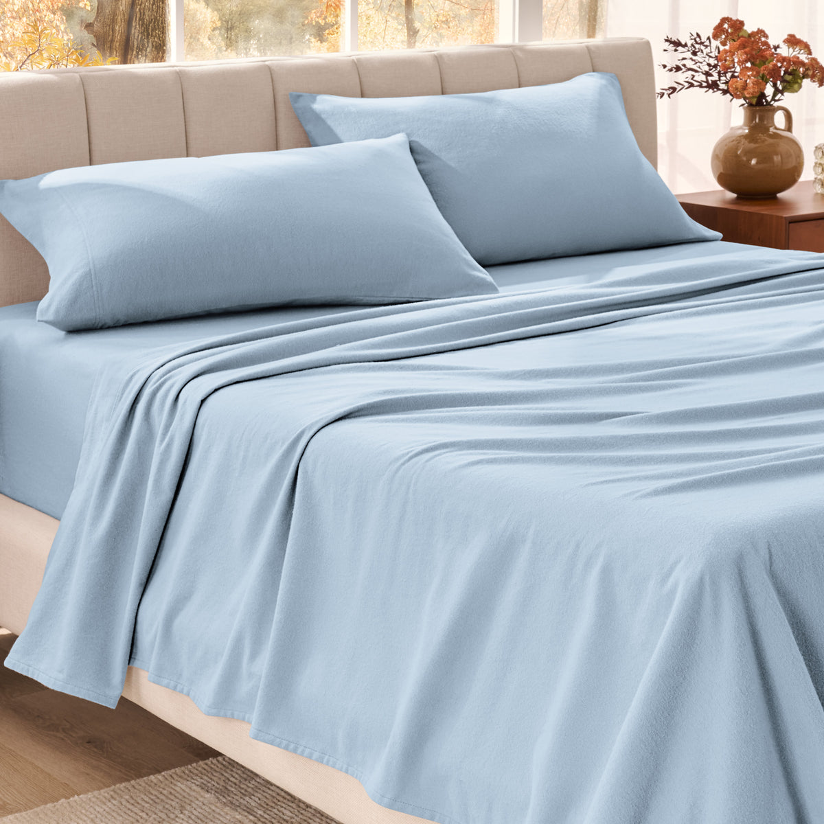 Bed sheets on a neatly made bed in a bright bedroom with large windows.