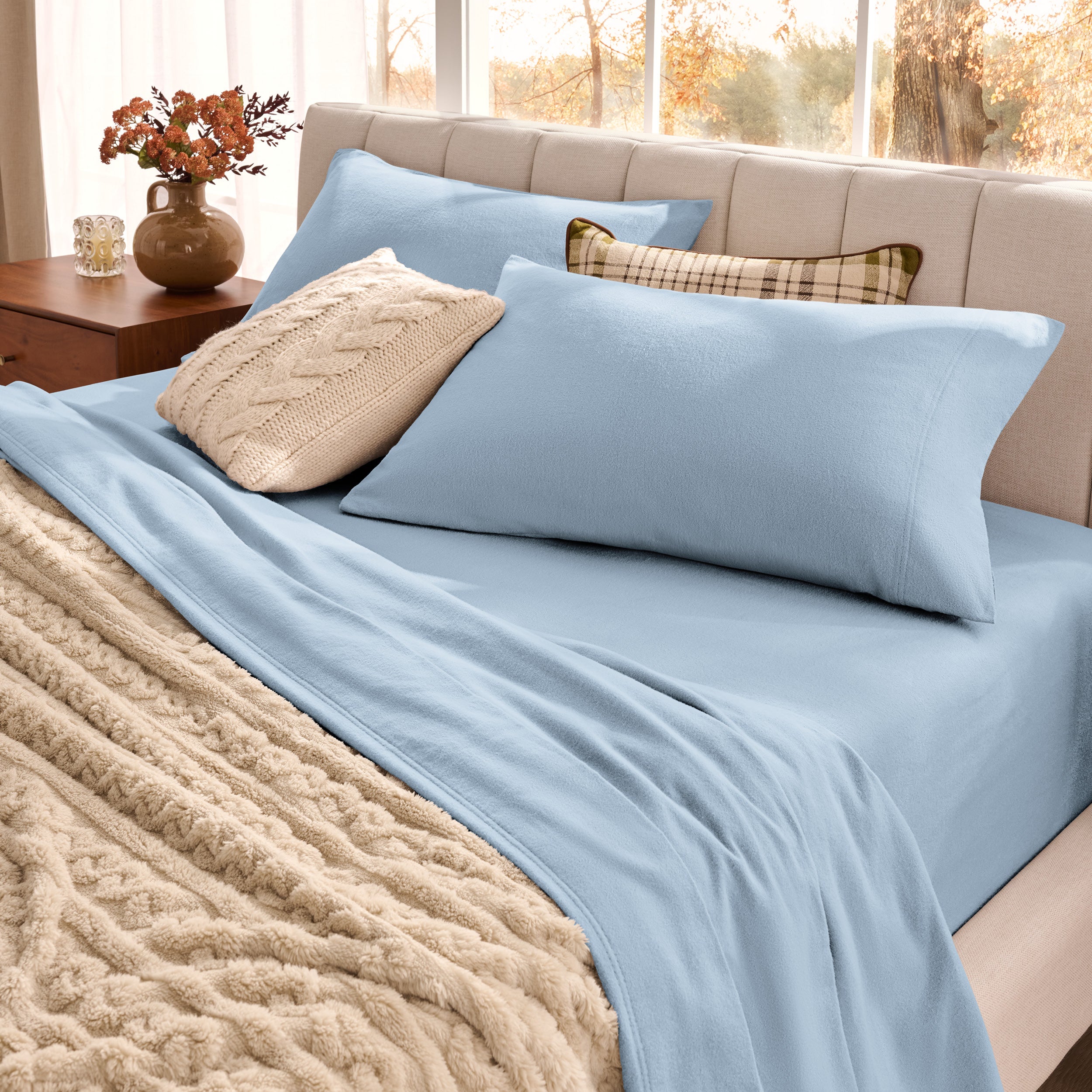 Neatly made bed with organic flannel sheets  and a beige blanket in a bright bedroom.