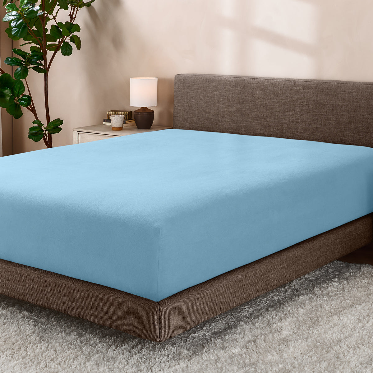 Bed with fitted sheet in a room with a lamp and plant.