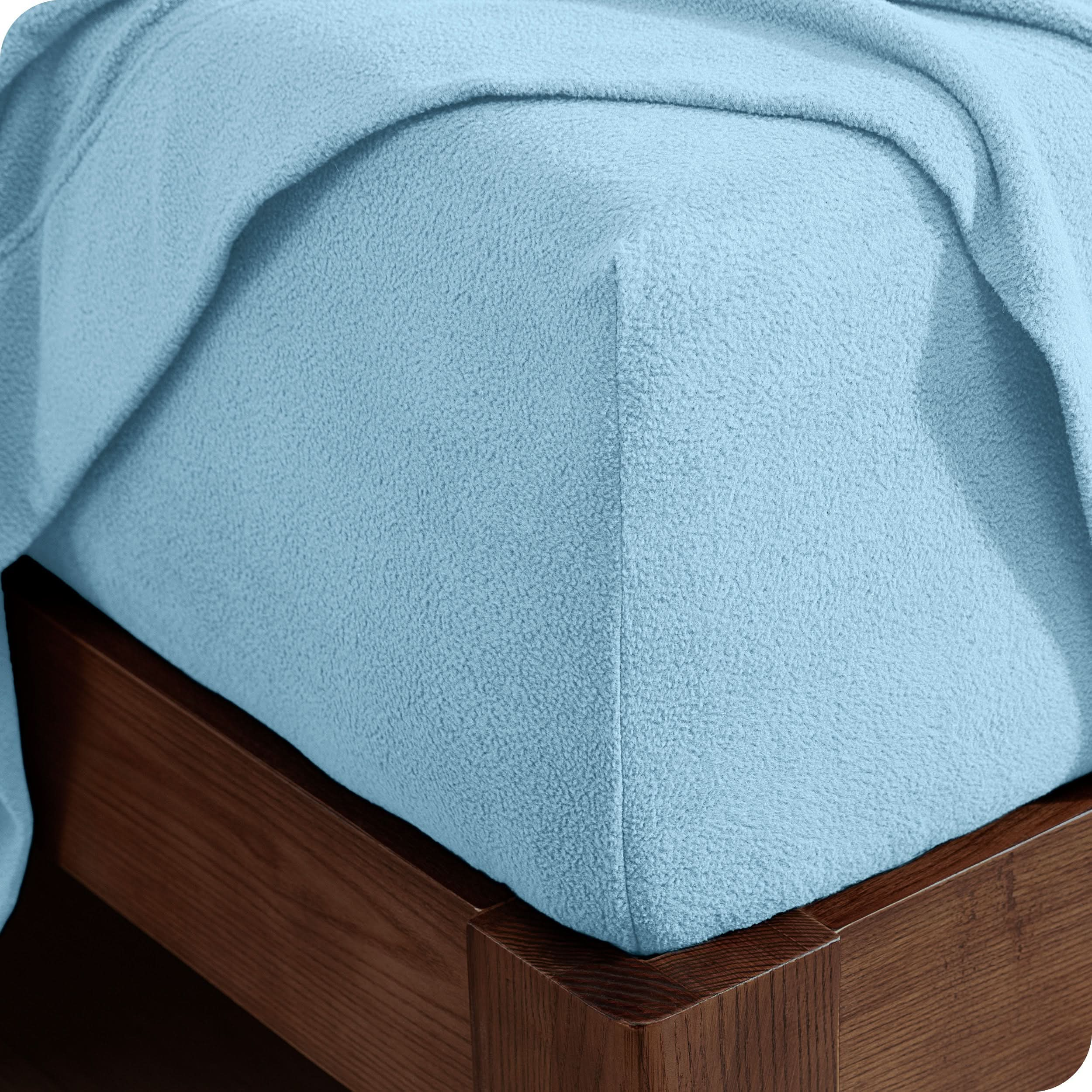 Corner of the bed with a fitted sheet on the mattress and a flat sheet draped over the side and end