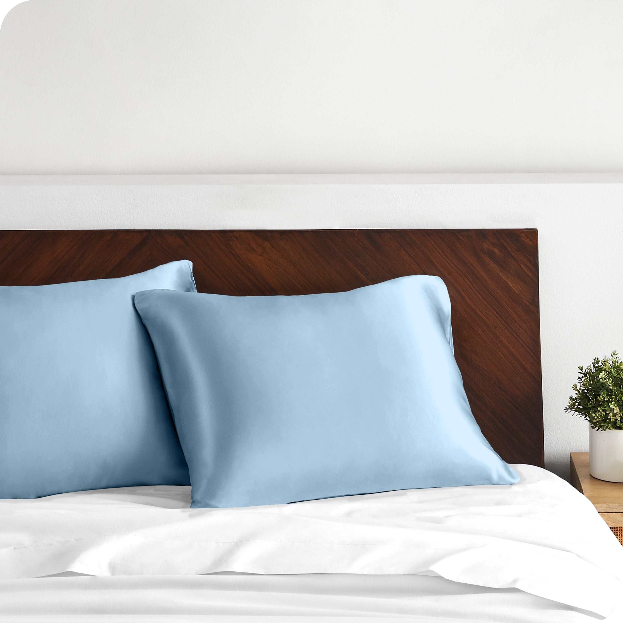 Two satin pillowcases on pillows against a wooden headboard