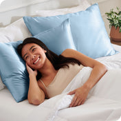 A woman is in bed and resting her head on a satin pillowcase